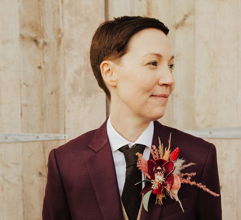 Ceri wears a burgundy wedding suit with a dried flower buttonhole