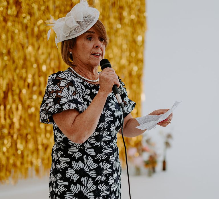 Wedding guest gives speech during reception in front of gold streamers wedding decor 