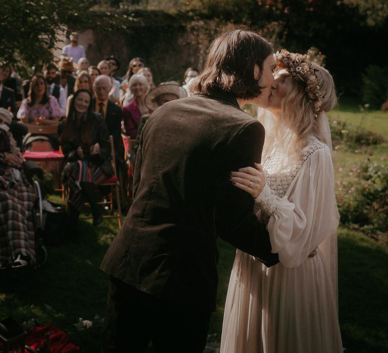 Blonde bridal in ethereal styled dress kisses her groom during outdoor wedding ceremony 