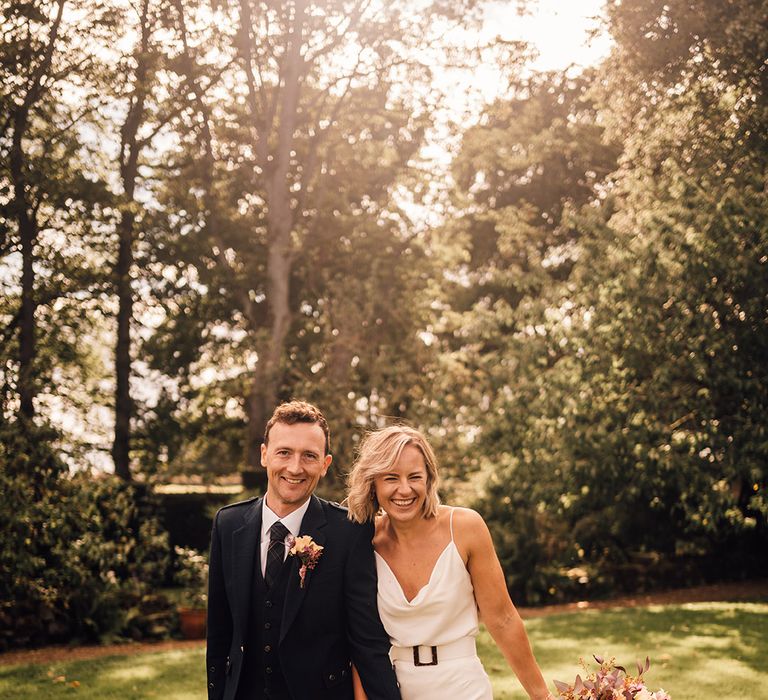 Bride wears cowl neck wedding dress with belt and holds tropical bouquet 