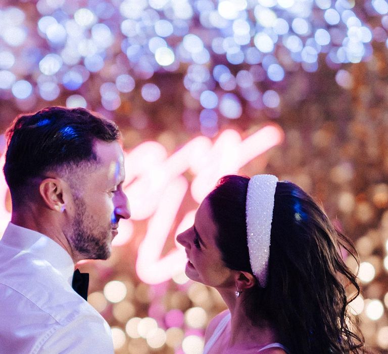 Bride with a sparkly thick white headband dances with the groom in a white shirt and black bow tie 