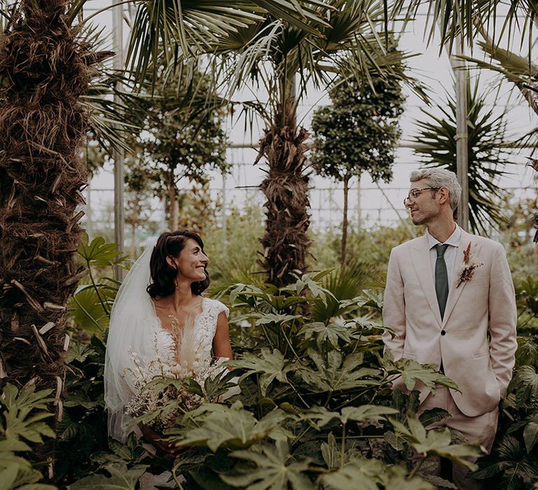 Couple pose and smile surrounded by plants and trees