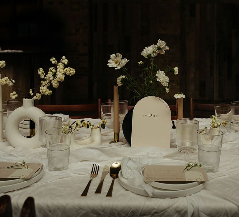 Monochrome wedding tablescape at 100 Barrington with rounded off white table numbers, black and white table decorations and vases, gold cutlery and white floral arrangements