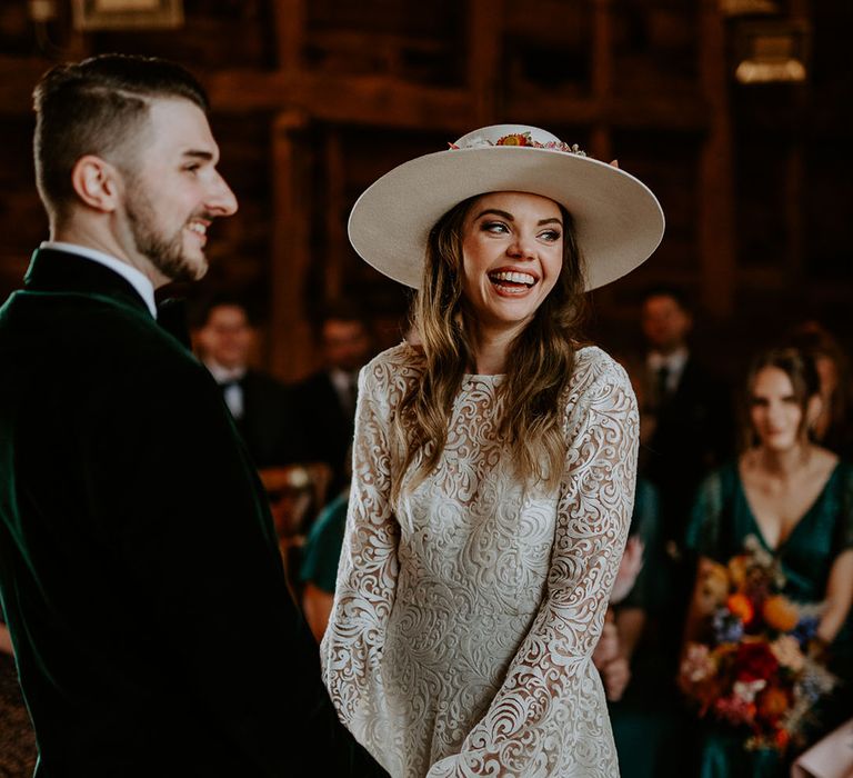 Groom in velvet suit jacket with the bride in bell sleeves with a white hat 