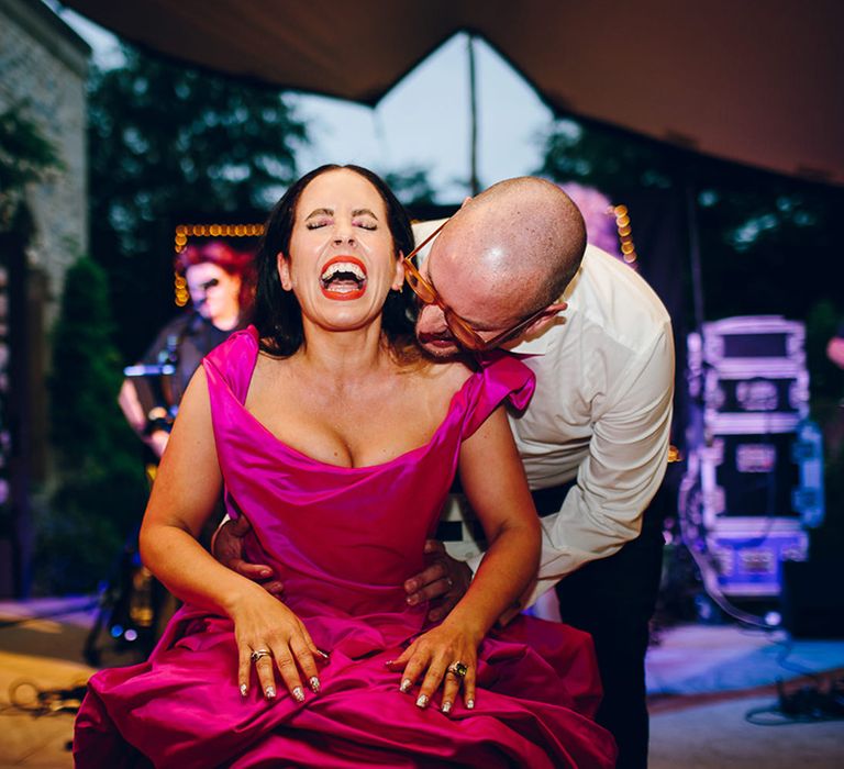 Bride in off the shoulder front ruching pink Vivienne Westwood wedding dress with groom in crisp white shirt behind her