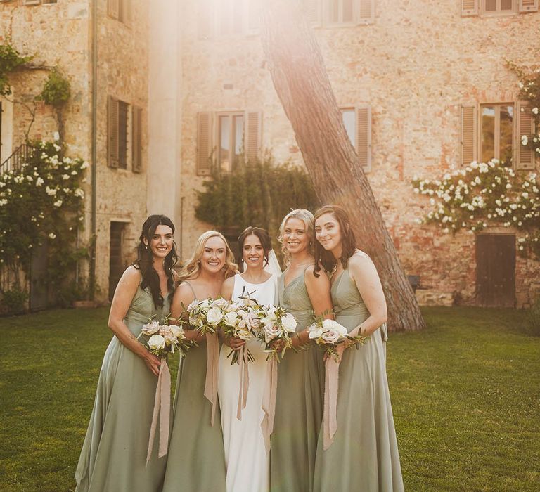 Win wedding photography from We Are // The Clarkes. This wedding photo shows a Bride in a simple white dress and her bridesmaids in sage bridesmaid dresses at golden hour