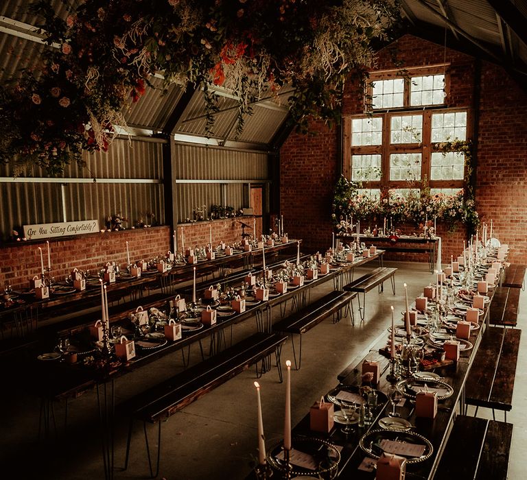 The Giraffe Shed reception room with long, luxe wedding tablescapes with tapered candles in gold candlestick holders and large rose and foliage hanging floral decor