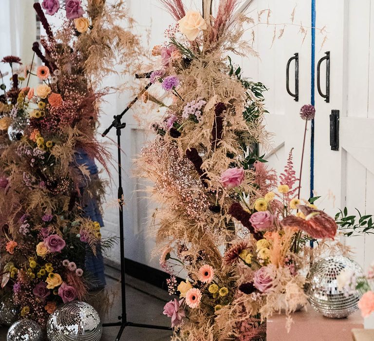 Roses, anthuriums, and dried grass in colourful boho flower column with disco ball decor 