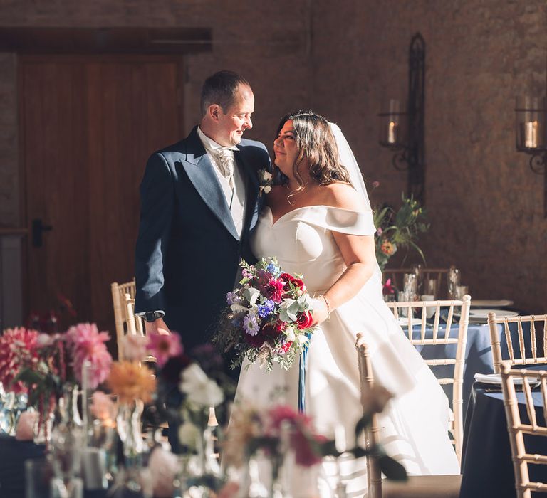 The sun shines in through the window onto the bride in an Essense of Australia wedding dress and the groom in a navy morning suit for the wedding at Stratton Court Barn Bicester