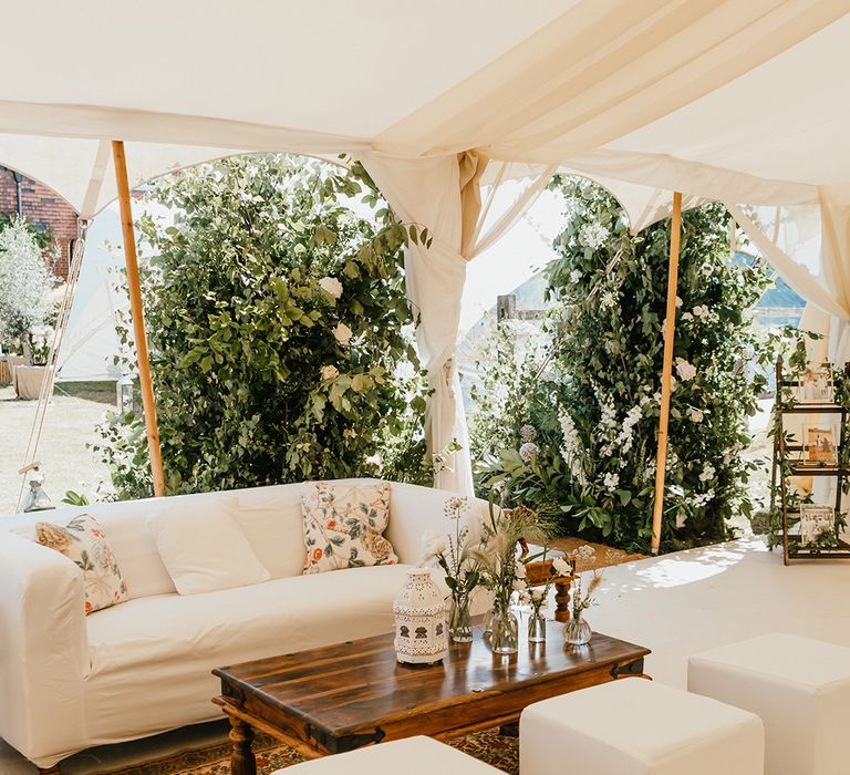 Chill out area within marquee finished with sofa, wooden table and colourful rug 