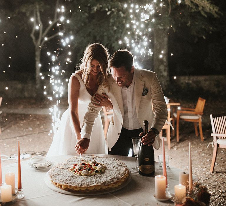 Bride & groom cut wedding cake surrounded by sparklers during outdoor wedding reception