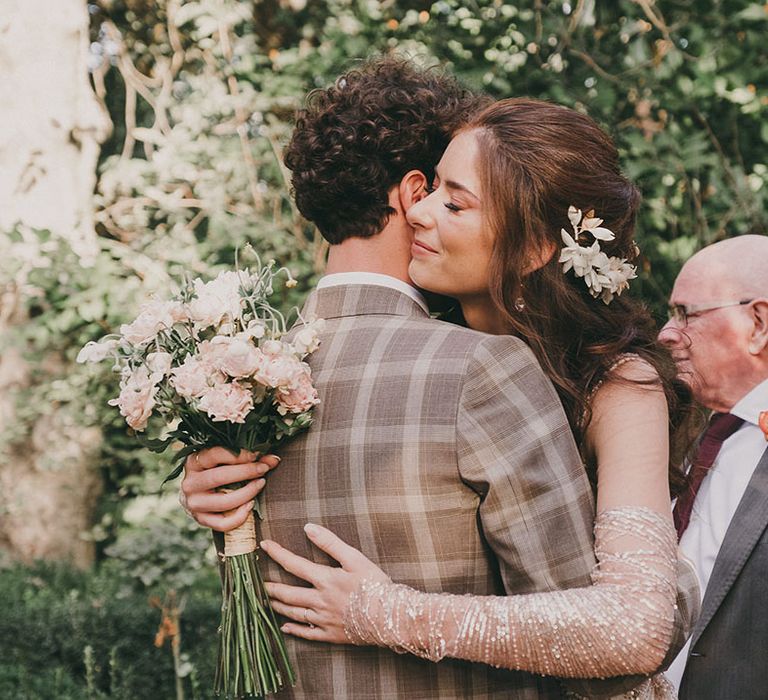 outdoor wedding ceremony in Spain with bride in a sparkly wedding dress embracing her husband in a check suit 