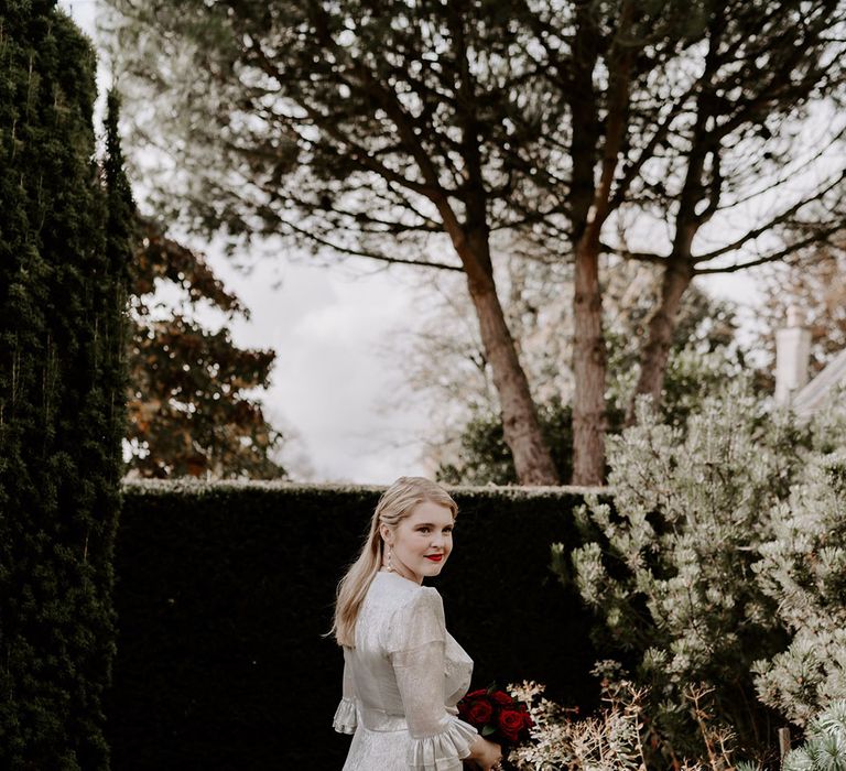 Bride with ruffle sleeves on silver metallic wedding dress with shoulder pads holding a red rose wedding bouquet 