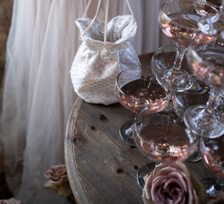 Bride holding shimmery white and silver bridal bag by pink champagne tower at Pentney Abbey wedding 