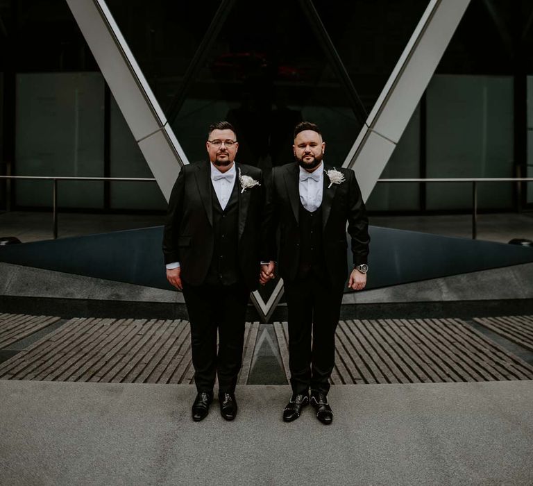 Grooms in complimenting three piece black tuxedos with off white bow ties, white garden rose, lavender twig and dried foliage boutonniere and grooms Louboutins shoes 