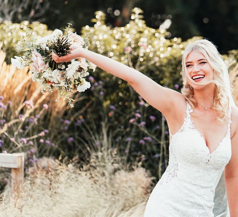 The bride in a lace wedding dress with thin straps and mermaid style skirt waving her wedding bouquet 