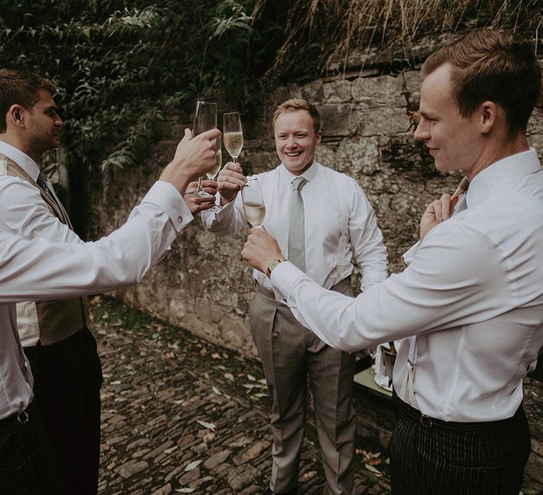 Groom and groomsmen wearing sage green tie having drinks of champagne for the morning of the wedding 