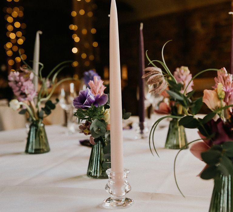 Pale pink, grey, and purple taper candles on the wedding table with tiny flower arrangements for decoration 