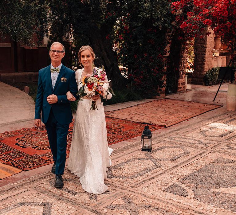 Groom in dark blue suit and light blue shirt with green bow tie walking arm in arm with the bride in modern lace separates 