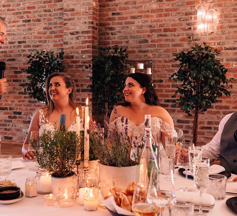 Two brides smile up at one of the father of the brides as he reads out his wedding speech 