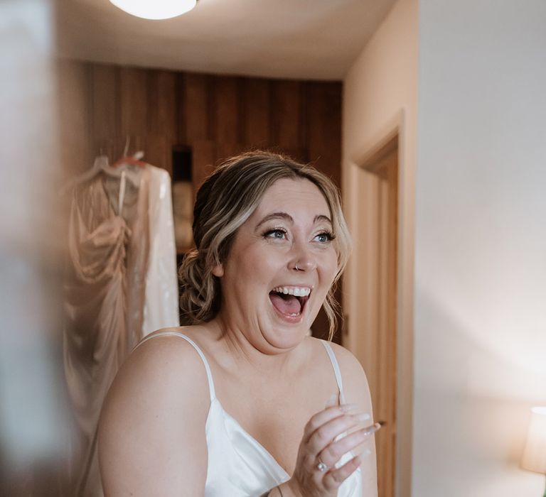 Bride pops open some champagne on the morning of the wedding in a white satin nightgown 