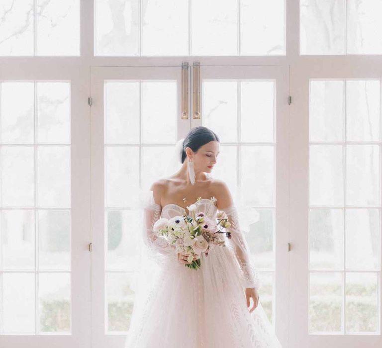 Bride wearing Bride at Notan inspired bridal editorial at Settrington Orangery wearing sweetheart neckline tulle mesh bridal gown with detachable puff tulle sleeves and delicate beading with cathedral length veil holding bridal bouquet with white poppies, light pink Persian buttercups, baby's-breath and foliage at Settrington Orangery