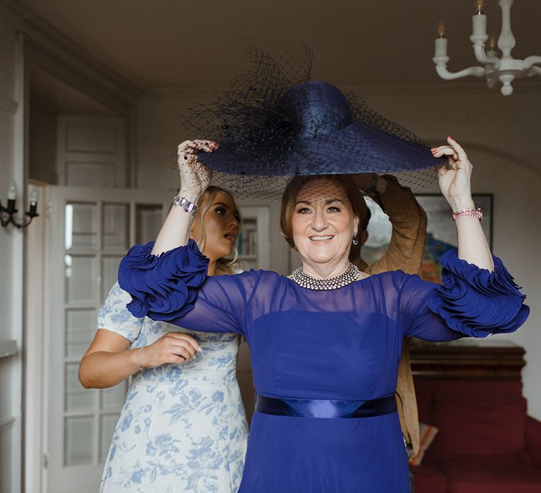 Mother of the bride puts on her dark blue hat wearing a dark blue dress for the wedding 