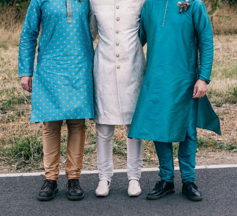 Groom in white and gold sherwani standing with groomsmen in traditional teal blue sherwanis 