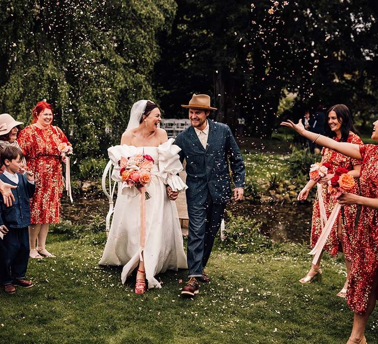 Bride in Jesus Peiro wedding dress walking with the groom in a double denim suit to confetti 