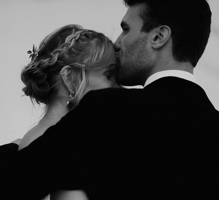 The groom romantically kisses the bride on the forehead in wedding photos 