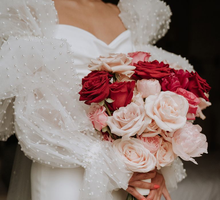 Pink and red rose wedding bouquet held by bride with statement puff pearl sleeves 