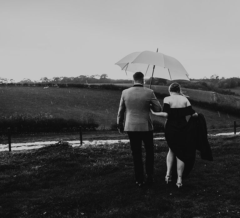 Rainy wedding day in October with the bride and groom walking in the fields with an umbrella 