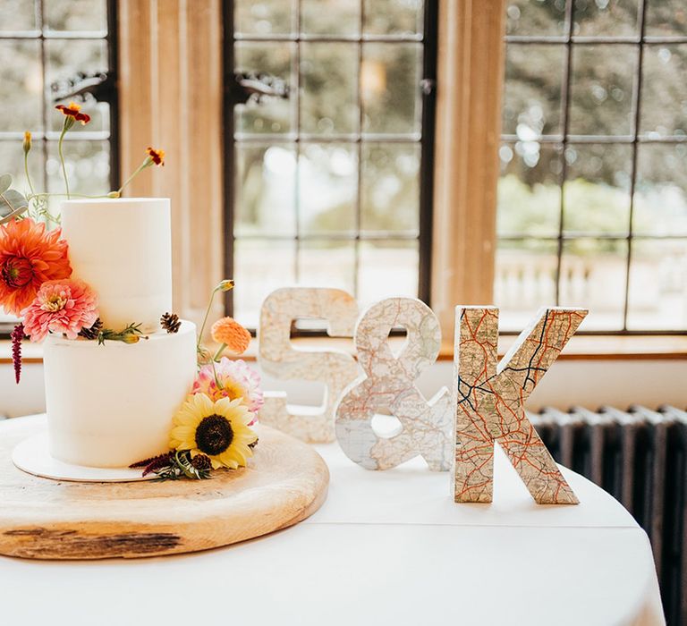 Two tier white iced wedding cake decorated with seasonal autumnal wedding flowers on table with initial decorations 