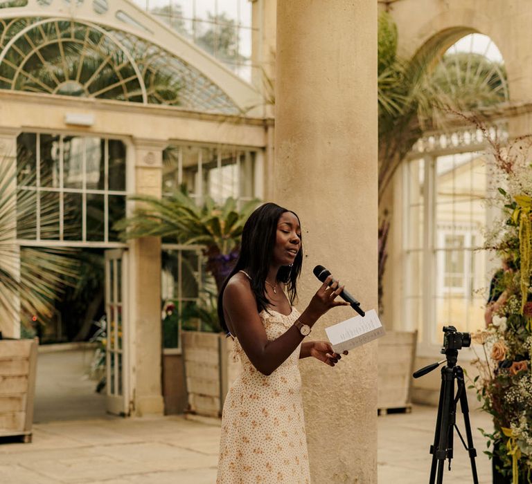 A wedding guest in floral dress performs a wedding reading at the religious wedding ceremony 