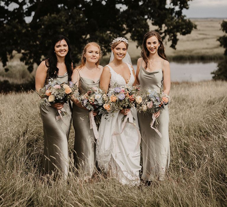 Bridal party with the bridesmaids in sage green satin bridesmaid dresses walking with the bride in a lace wedding dress 