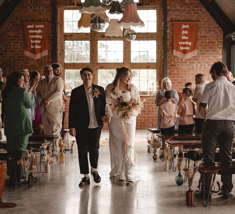 Brides walking back down the aisle together at 70s retro wedding 