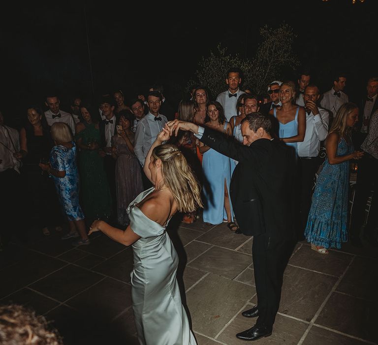 Bride in off the shoulder wedding dress with groom in black tuxedo having their first dance at destination wedding 