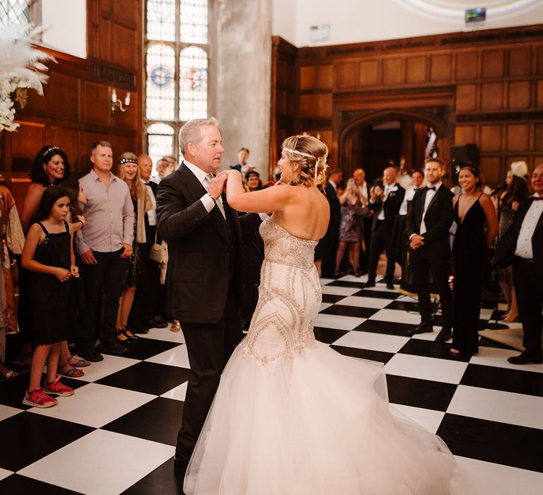 Bride in mermaid wedding dress with groom in black suit have their first dance together on black and white checkered dance floor 