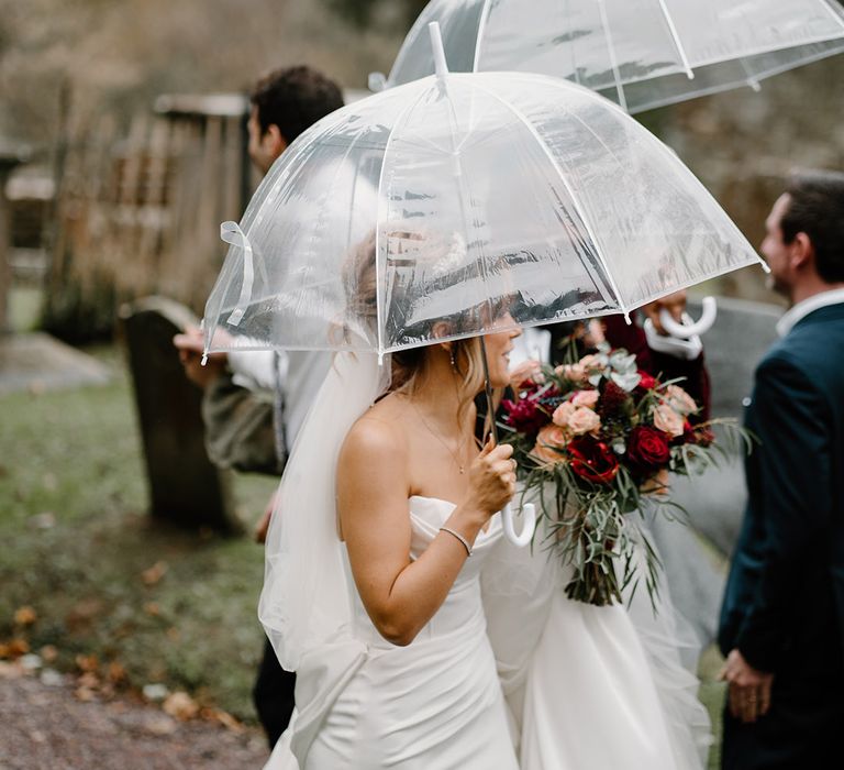 Rainy wedding day with the bride and groom walking with clear umbrellas 