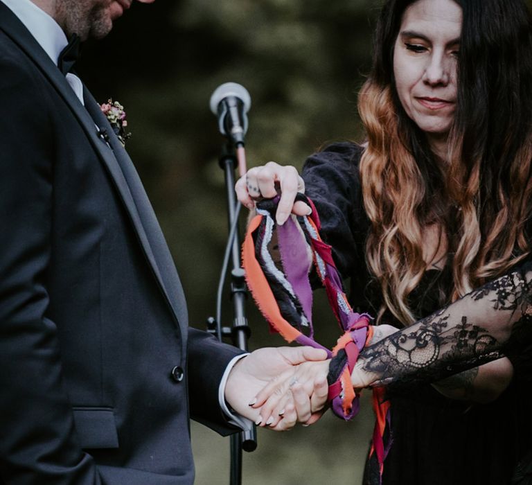 Handfasting wedding ceremony with the bride and groom's hands being tied together with fabric 