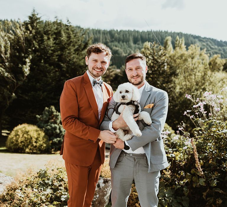 Two grooms holding their fluffy pet dog at rustic wedding 