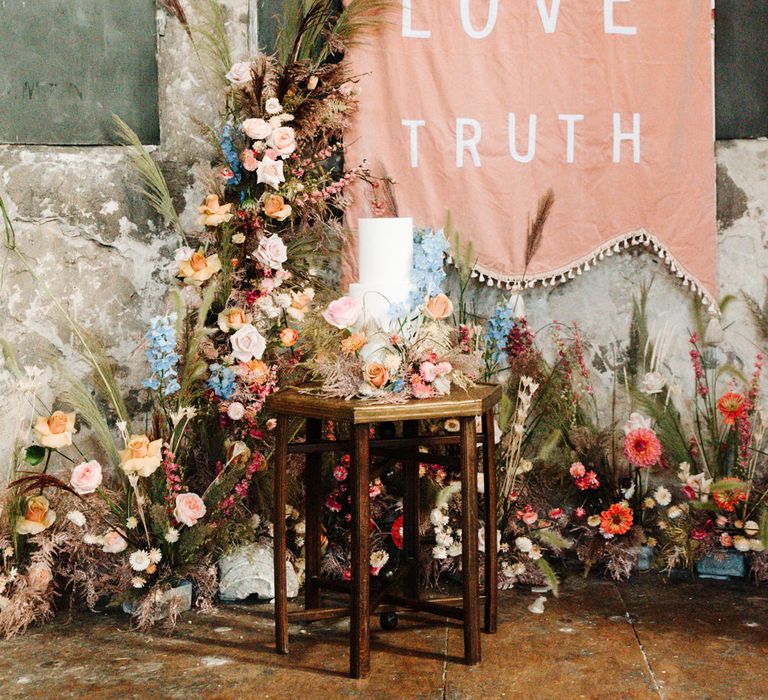 Wedding cake display in front of a fabric wedding sign and bright wedding flowers 