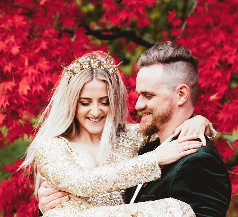 Bride being picked up by groom in woodland setting with red trees in the background. Photography by Maryanne Weddings.