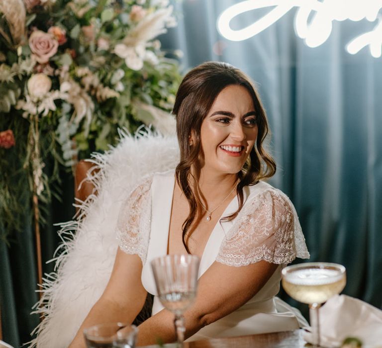 Side shot photograph of bride on her wedding day with champagne coupe and neon sign 