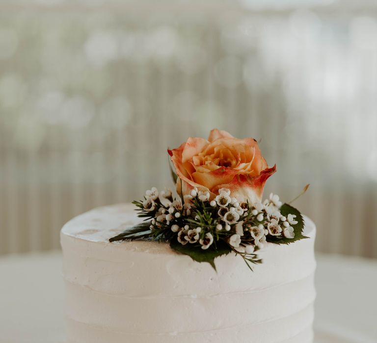 Single tier buttercream iced wedding cake with orange wedding flower decor 