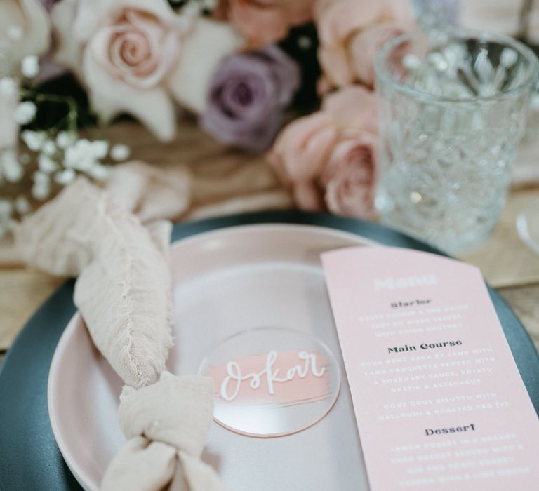 Place setting with black charger plater, pink menu card and acrylic name place card 