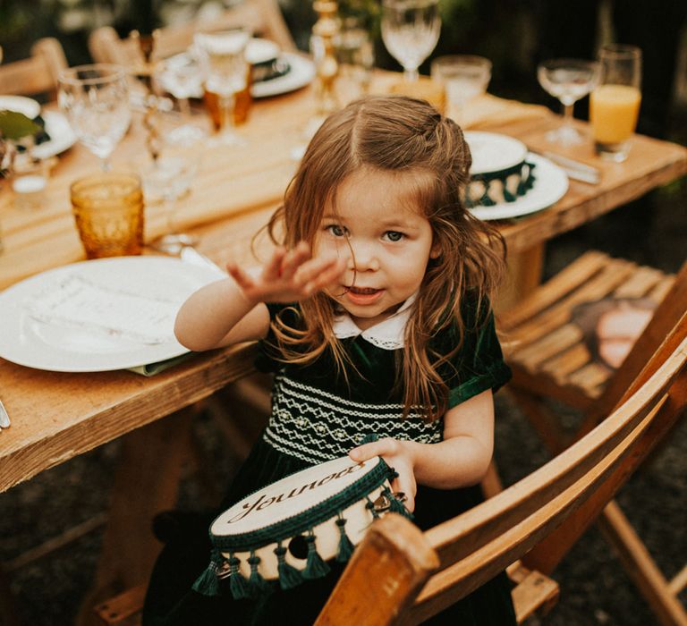 Little wedding guest in a dark green velvet dress playing with her tambourine wedding favour