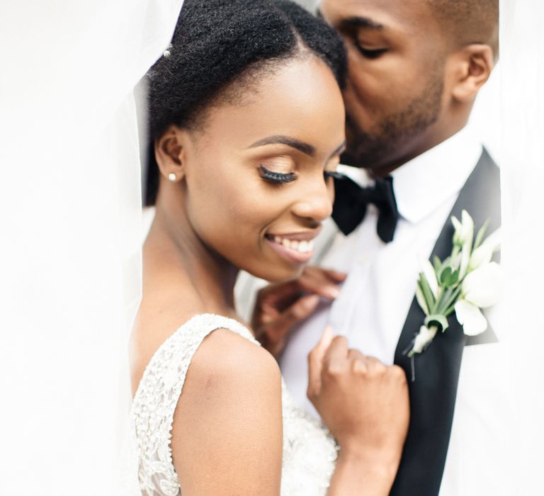 Bride looks down as groom kisses her cheek 