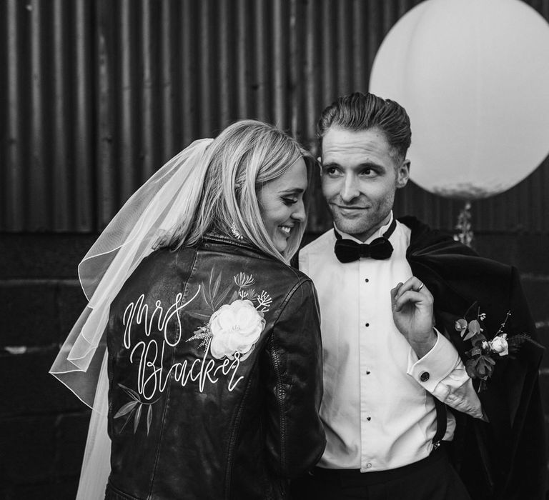 Bride in personalised leather bridal jacket and veil holding hands with groom in braces and bow tie at Caswell House wedding