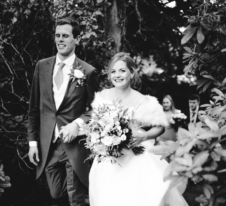 Bride & groom laugh whilst walking together on wedding day